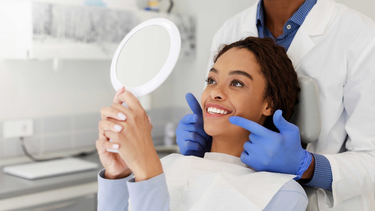 Reviewing the result of a cleaning in Orlando Patient checking her smile in a hand mirror while her dentist points out an area in Orlando