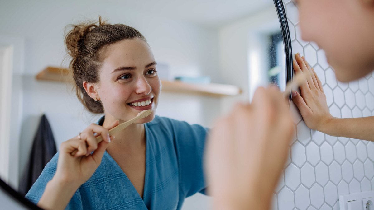 Patient brushing her teeth carefully in front of a bathroom mirror while recovering from a tooth extraction