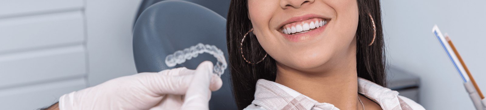 A smiling adult patient holding a clear Invisalign aligner at a dental visit
